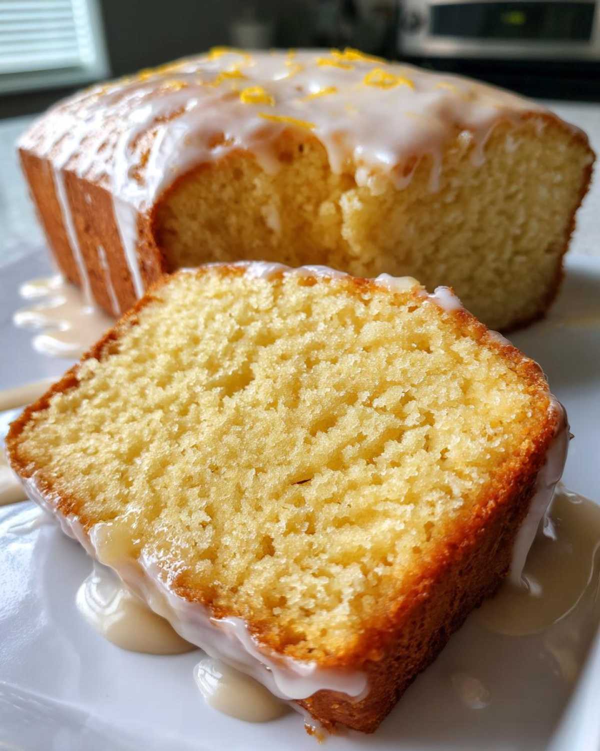 Close-up of a moist slice of lemon pound cake covered in white glaze and lemon zest.
