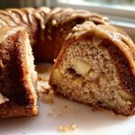 Close-up of a slice cut from a moist apple bundt cake, showing apple chunks inside and drizzled with caramel glaze.