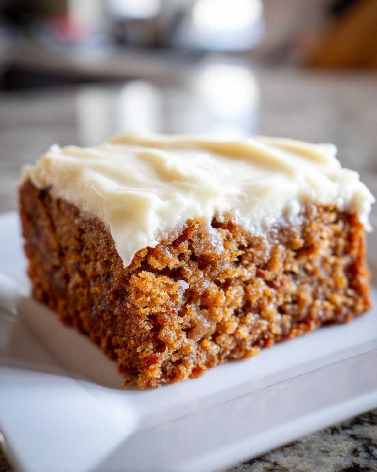 Close-up of a moist slice of applesauce cake topped with thick, white cream cheese frosting.