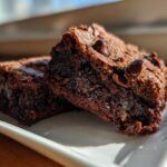 Close-up of two fudgy black bean brownies with visible chocolate chips on a white plate.