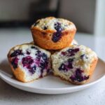 Close-up of three moist blueberry protein muffins, one cut in half showing the berry-filled interior.