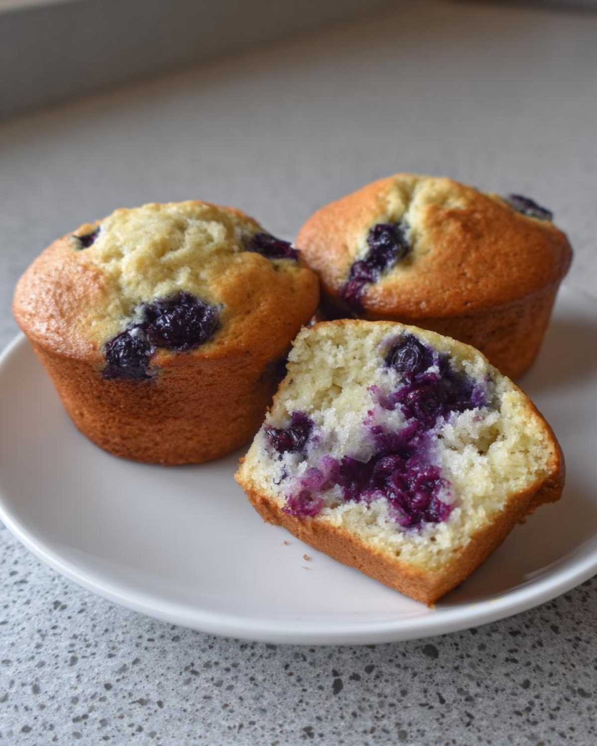 Close-up of three moist blueberry protein muffins, one cut in half showing the vibrant purple interior.