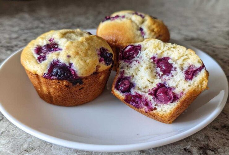 Three moist blueberry protein muffins, one cut in half showing the fluffy interior and berries.