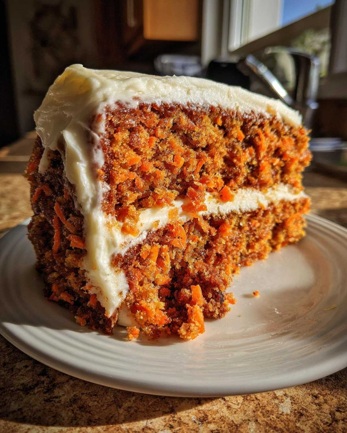 Close-up of a moist slice of carrot cake recipe showing visible shredded carrots and thick cream cheese frosting.