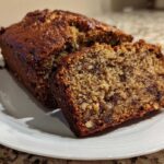A slice cut from a loaf of moist date nut bread showing visible dates and walnuts.