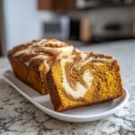 A close-up of a thick slice of moist pumpkin cream cheese bread showing the beautiful orange and white swirl.