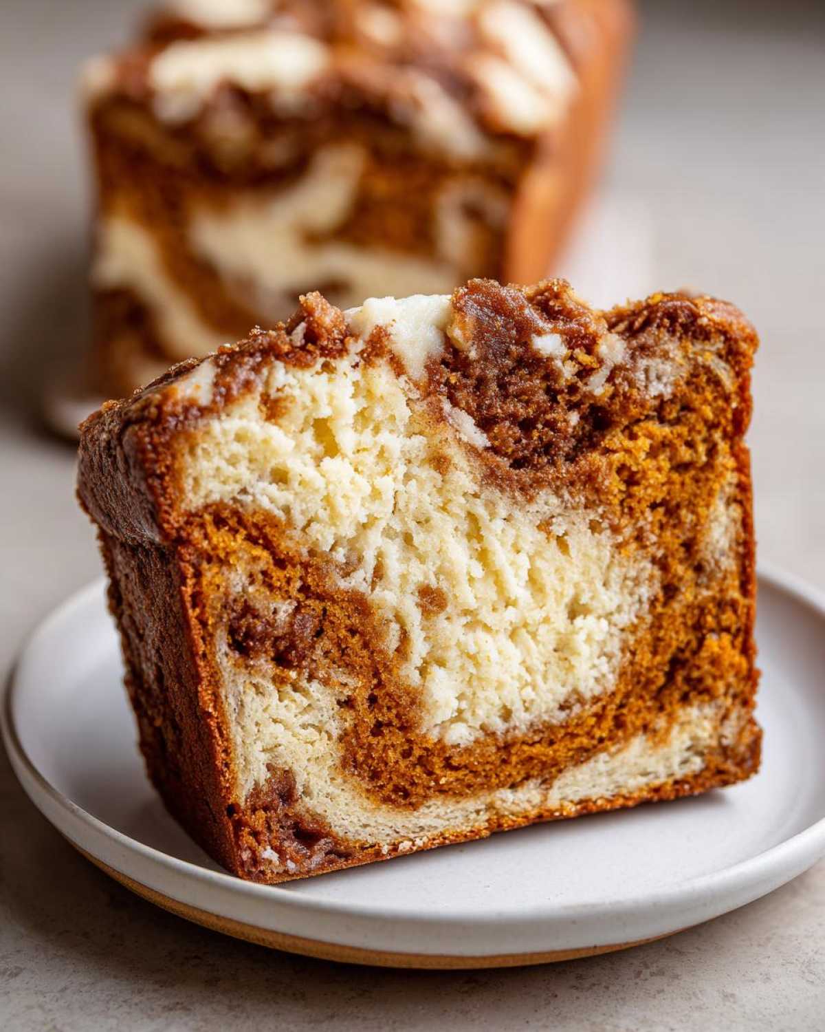 Close-up of a moist slice of pumpkin cream cheese bread showing the swirl of pumpkin and cream cheese layers.