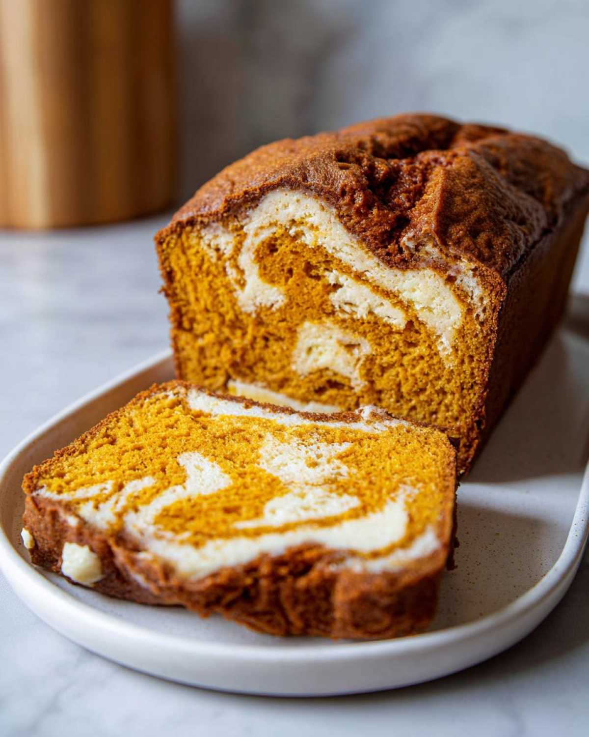 A loaf of moist pumpkin cream cheese bread, partially sliced to show the orange pumpkin batter swirled with white cream cheese filling.