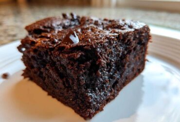 A close-up of a rich, dark, fudgy slice of sweet potato brownies on a white plate.