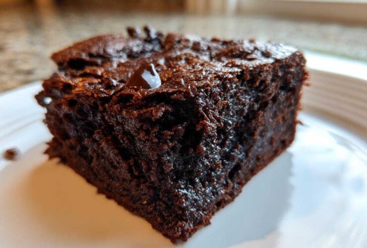 A close-up of a rich, dark, fudgy slice of sweet potato brownies on a white plate.