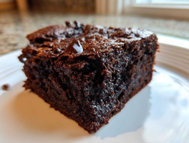 A close-up of a rich, dark, fudgy slice of sweet potato brownies on a white plate.
