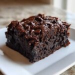 A close-up of a rich, dark chocolate square of sweet potato brownies topped with melted chocolate chips.