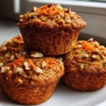 A close-up stack of three delicious morning glory muffins topped with shredded carrots and chopped pecans.