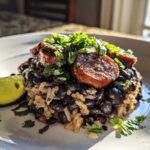 A close-up serving of 1-Pot black beans and rice topped with sliced sausage and fresh cilantro, with a lime wedge on the side.
