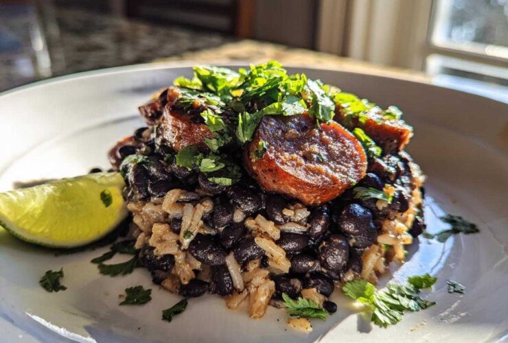 A close-up serving of 1-Pot black beans and rice topped with sliced sausage and fresh cilantro, with a lime wedge on the side.