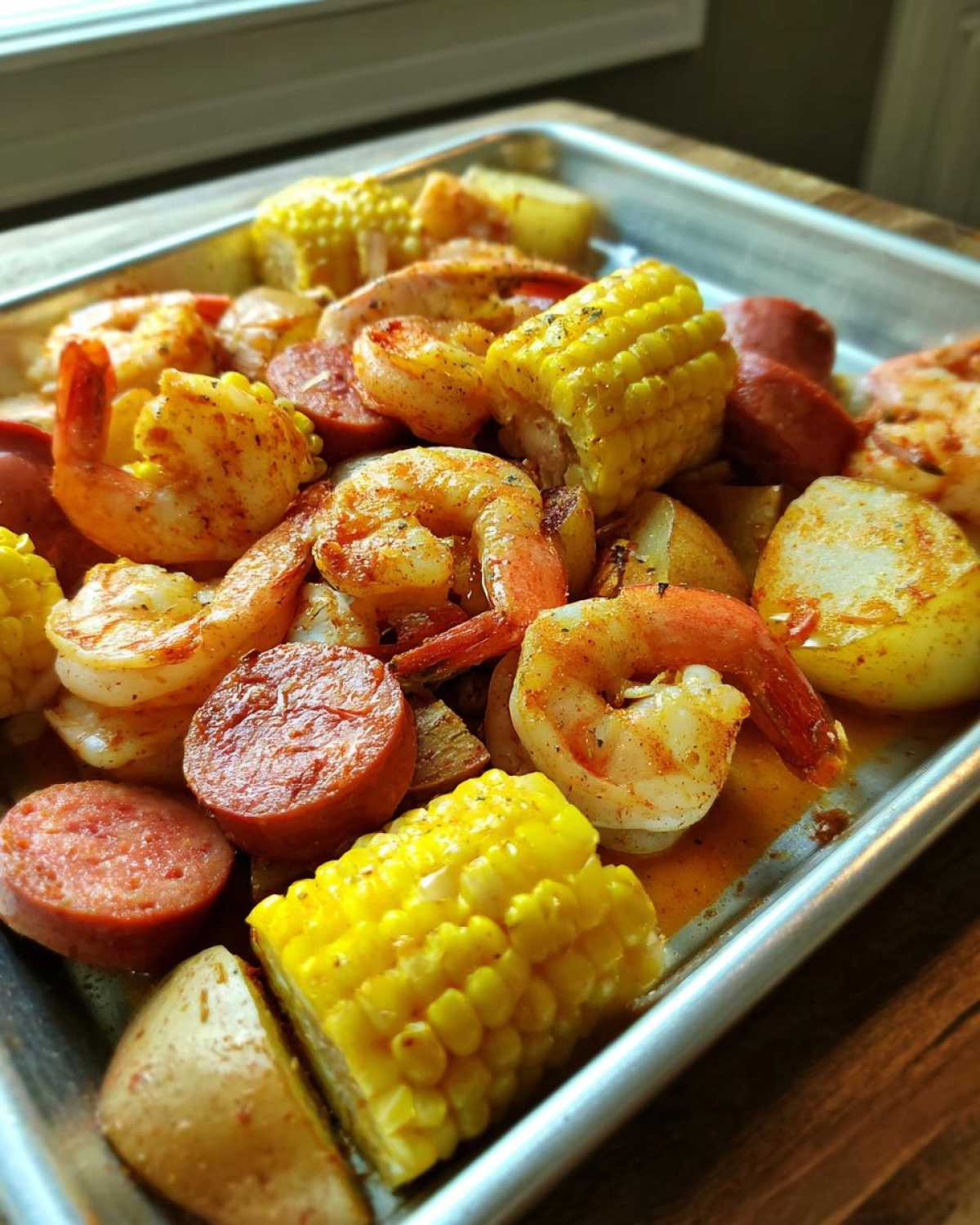 Close-up of seasoned shrimp, sausage slices, corn on the cob, and potatoes ready for an oven shrimp boil.