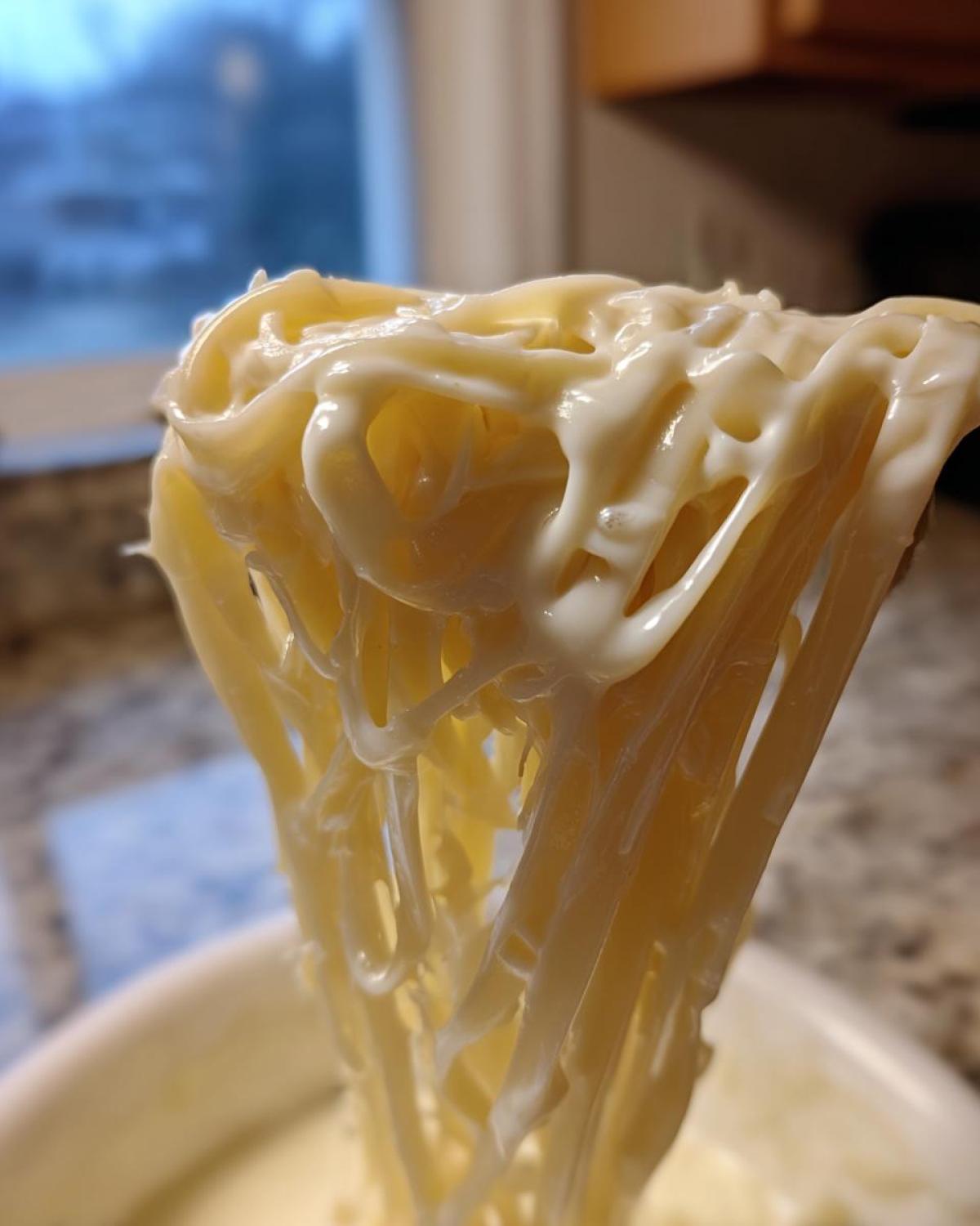 Close-up of fettuccine pasta thickly coated in creamy Olive Garden Alfredo sauce being lifted by a utensil.
