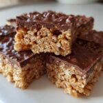 Close-up of several squares of peanut butter rice krispie treats topped with a thick layer of melted chocolate.