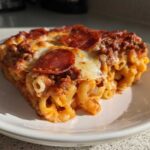 A close-up serving of baked pizza pasta featuring macaroni, meat sauce, melted cheese, and pepperoni slices.