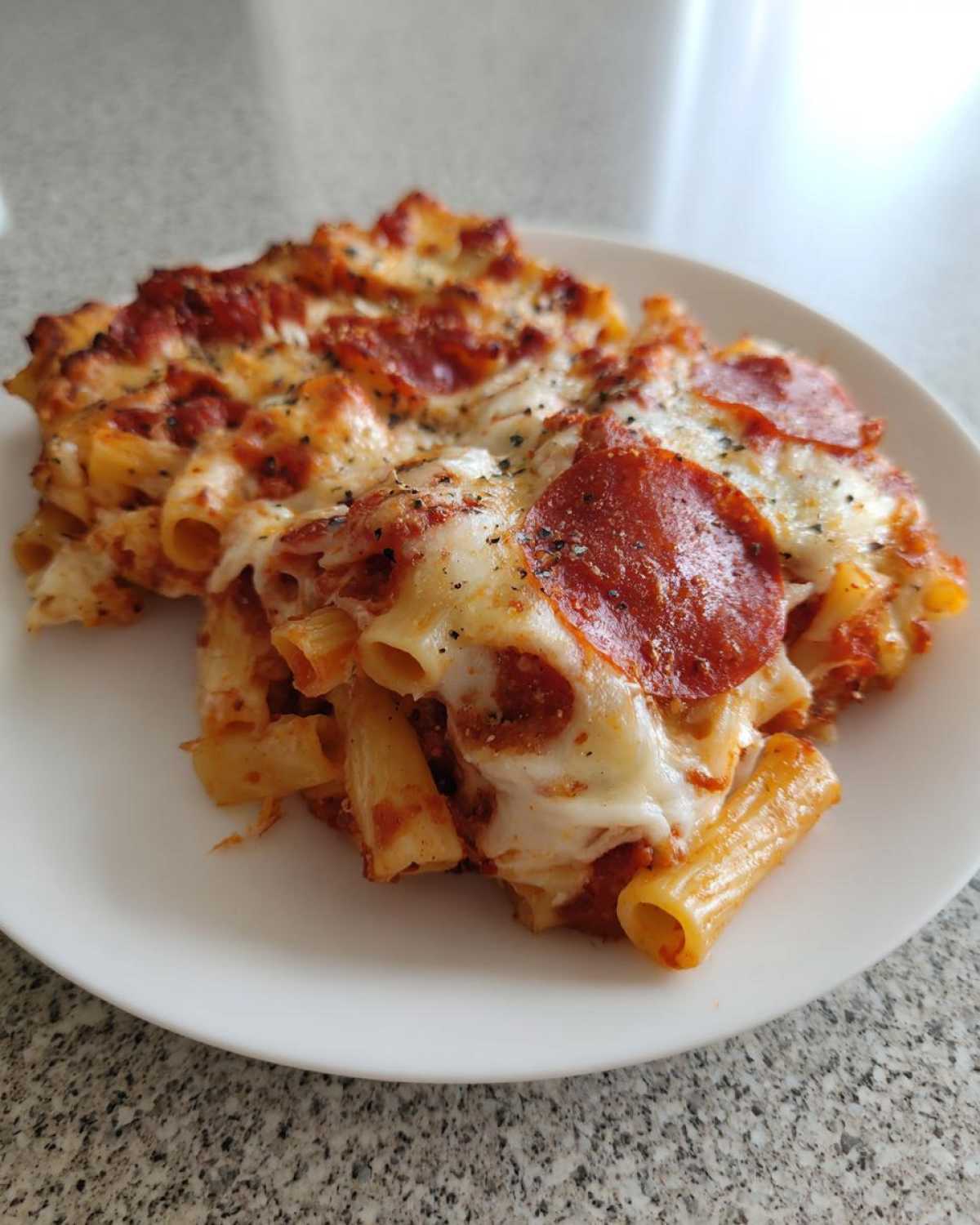 A generous serving of baked pizza pasta featuring rigatoni noodles, melted mozzarella, and pepperoni slices.