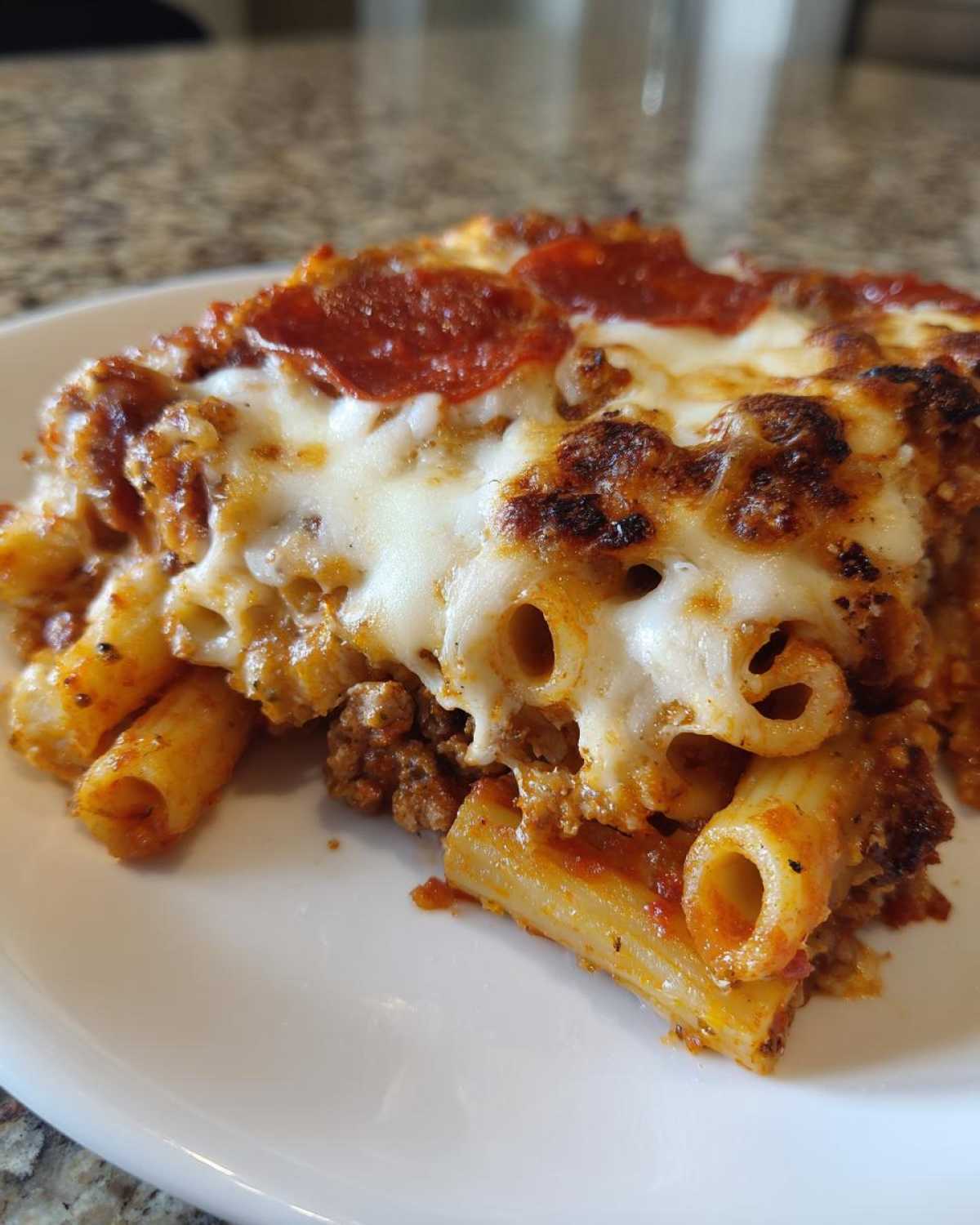 Close-up of a serving of pizza pasta bake featuring ziti pasta, meat sauce, melted cheese, and pepperoni slices.