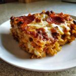 A close-up shot of a hearty slice of pizza pasta bake topped with melted mozzarella and pepperoni slices.