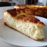 A thick slice of creamy Protein Cheesecake with a golden-brown baked top, served on a white plate.