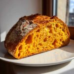 Close-up of a vibrant orange pumpkin sourdough loaf, showing an open, airy crumb structure, sliced in half.