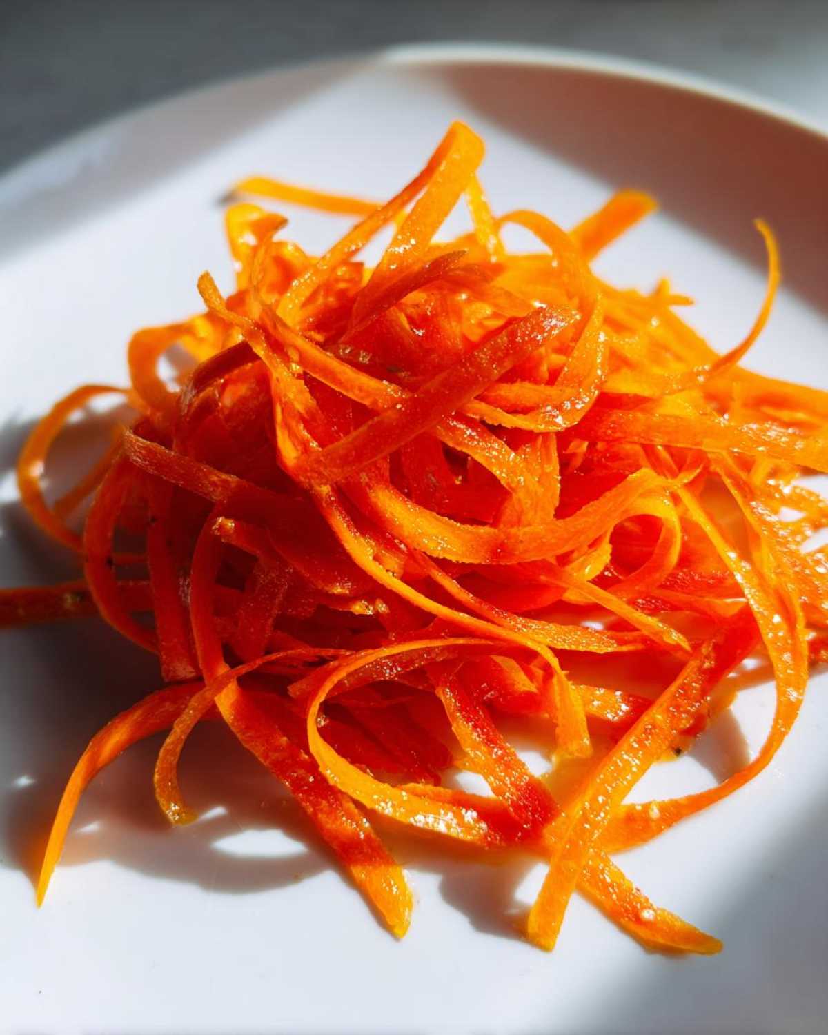 Close-up of bright orange, thinly shaved ribbons of carrot, ready for a raw carrot salad.