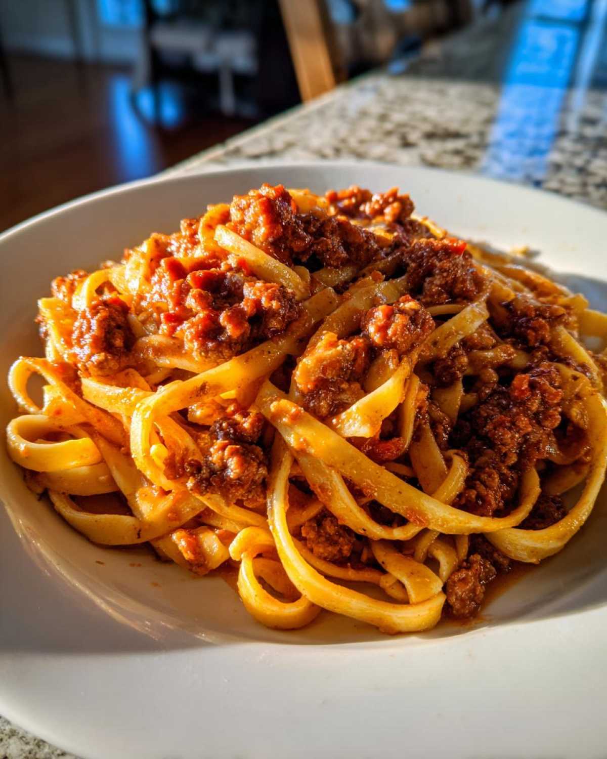 Close-up of fettuccine pasta generously topped with rich, meaty bolognese sauce, served on a white plate.