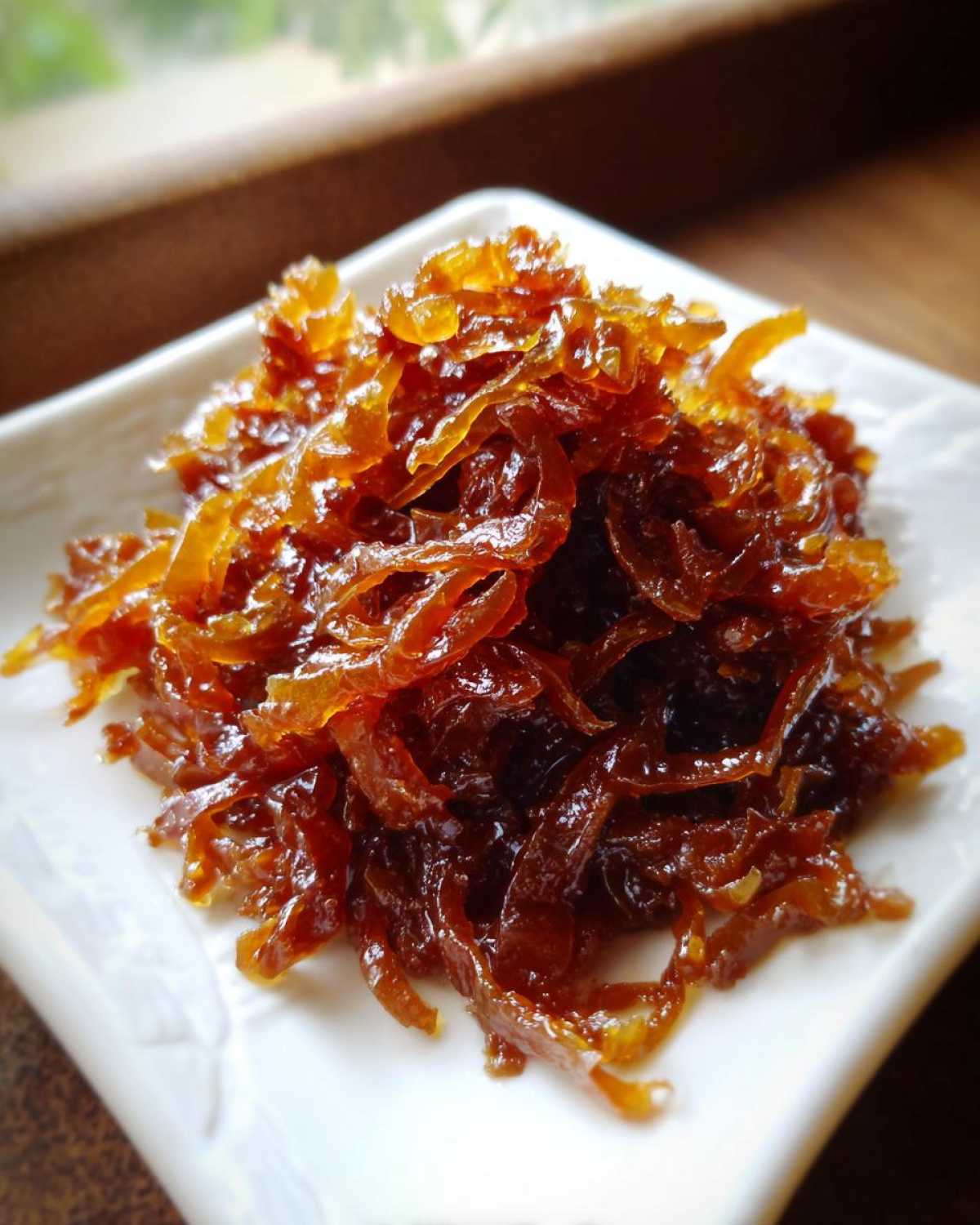 A close-up of deeply browned, glossy caramelized onions piled on a small white serving dish.