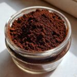 Close-up of rich, dark brown hot cocoa mix powder filling a small, clear glass jar.