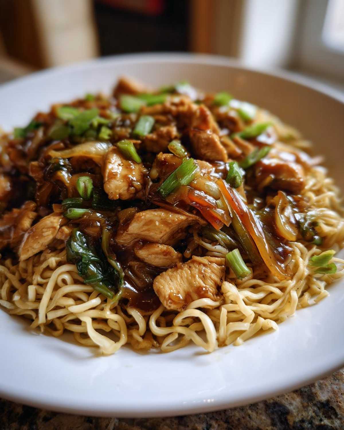 Close-up of a bowl filled with a savory chicken chow mein recipe, featuring noodles, sliced chicken, vegetables, and green onions.