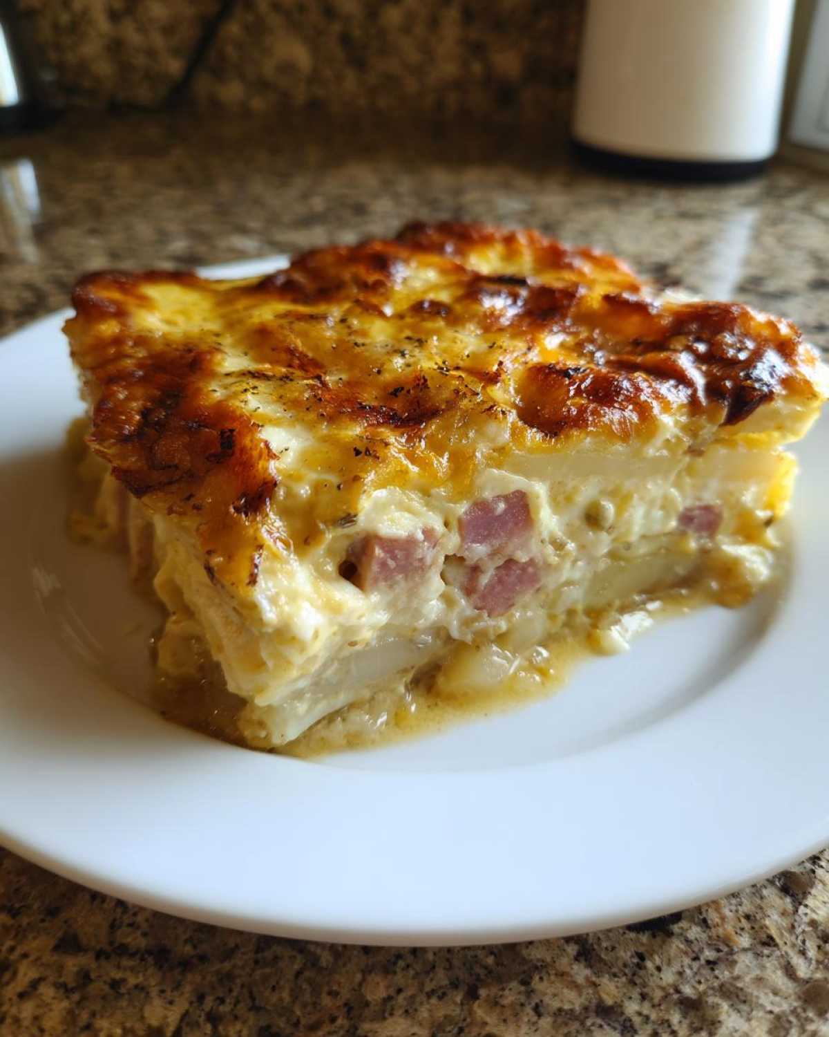A generous slice of creamy scalloped potatoes and ham with a golden, bubbly, cheesy crust served on a white plate.