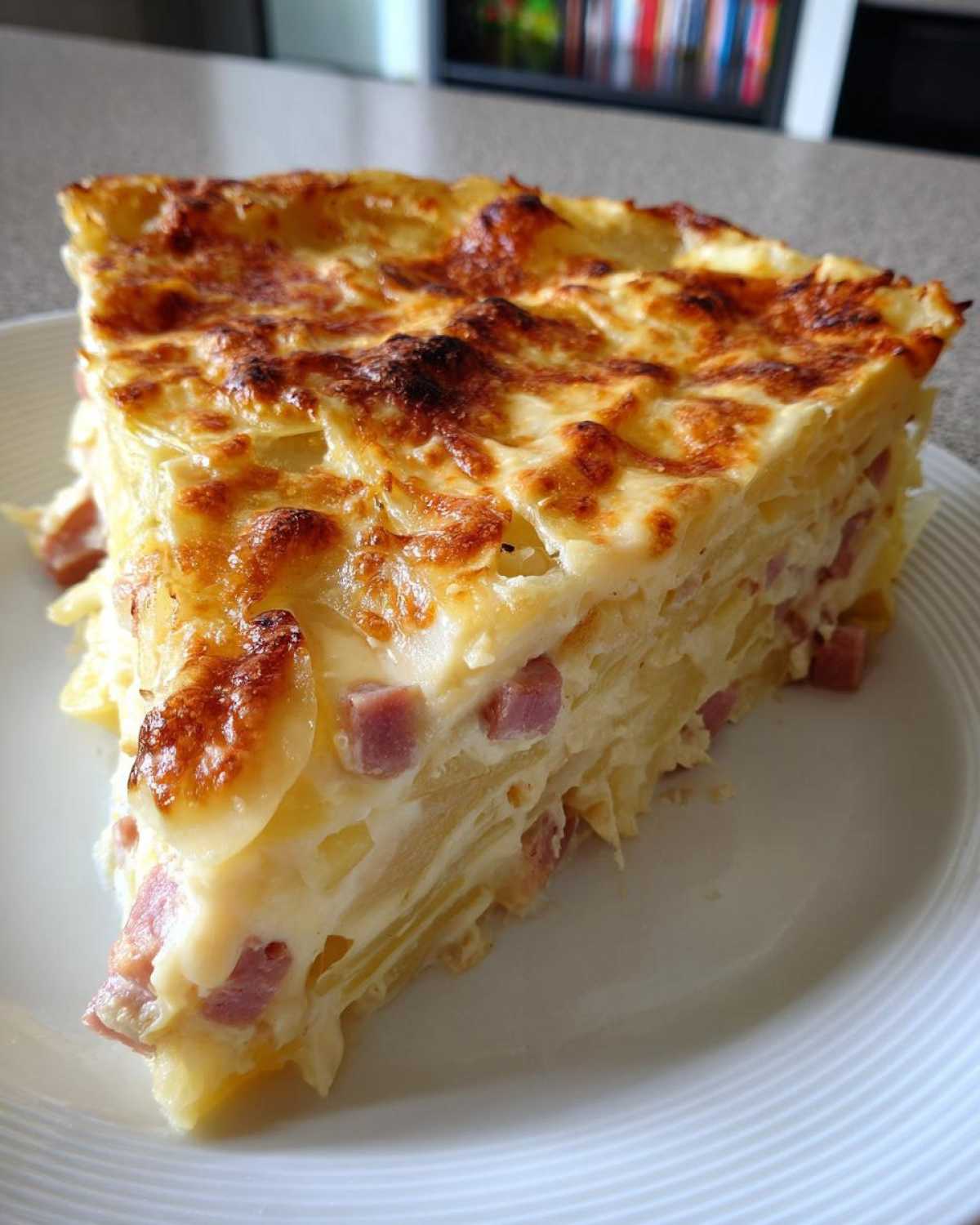 A tall, golden-brown slice of scalloped potatoes and ham, showing layers of potato, ham cubes, and creamy sauce.