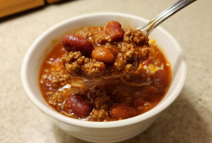 A spoonful of rich, meaty crockpot chili, featuring kidney beans and ground beef, lifted from a white bowl.