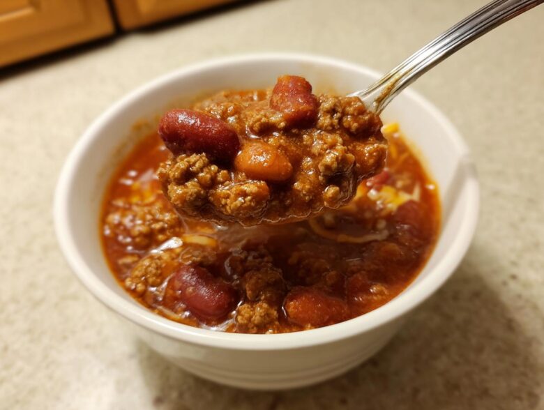 A spoonful of rich, meaty crockpot chili, featuring kidney beans and ground beef, lifted from a white bowl.