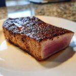 A close-up of a perfectly seared tuna steak, showing a dark crust and a rare, pink center, prepared with a MARINADE FOR TUNA STEAK.