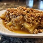Close-up of a serving of warm apple crisp with a thick, golden oat topping and bubbling, syrupy apple filling.
