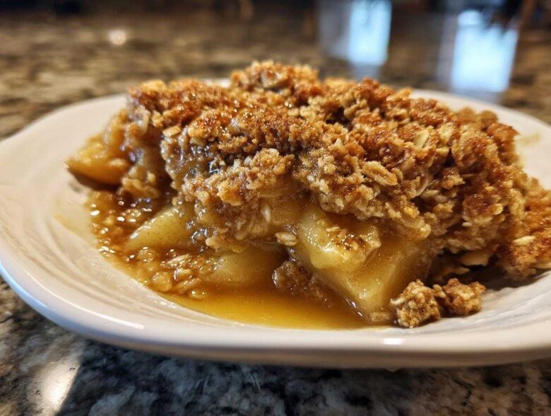 Close-up of a serving of warm apple crisp with a thick, golden oat topping and bubbling, syrupy apple filling.