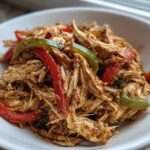 Close-up of shredded chicken mixed with red and green bell peppers, seasoned for crockpot chicken fajitas.