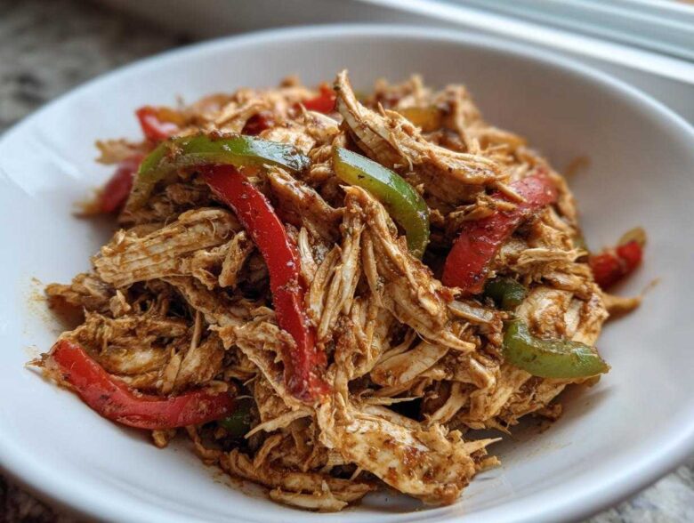 Close-up of shredded chicken mixed with red and green bell peppers, seasoned for crockpot chicken fajitas.