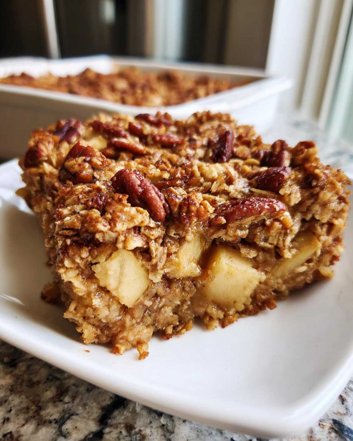 Close-up of a square slice of baked oatmeal with chunks of apple and topped with pecans.