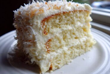 Close-up of a moist slice of 3-layer coconut cake covered in white frosting and shredded coconut.
