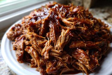 A close-up view of a generous mound of saucy, shredded Slow Cooker Pulled Pork piled high on a white plate.