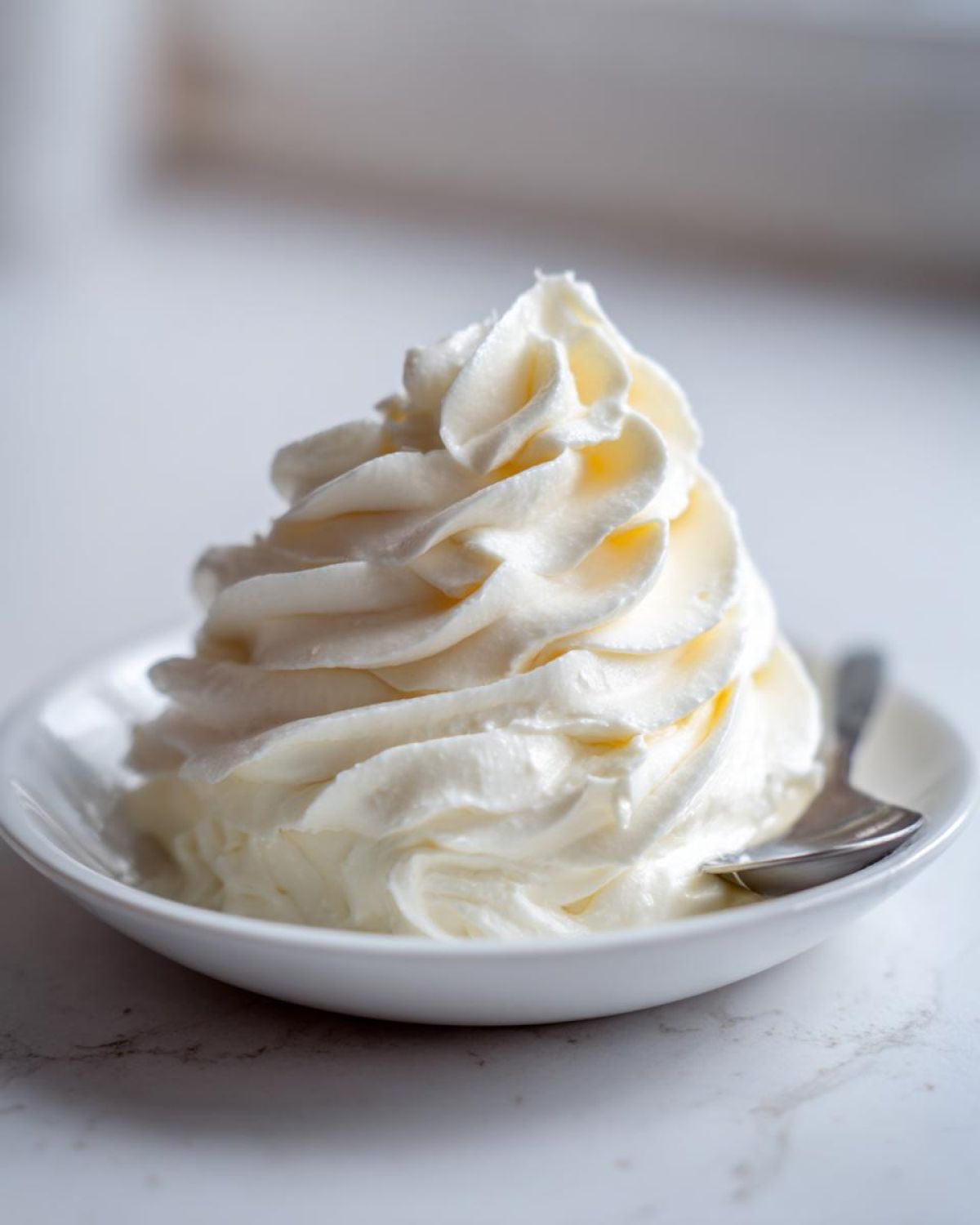 A close-up of a perfectly piped swirl of smooth cream cheese frosting in a small white bowl.