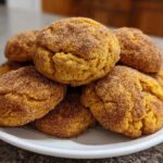 A close-up stack of soft, orange pumpkin snickerdoodle cookies heavily coated in cinnamon sugar, resting on a white plate.