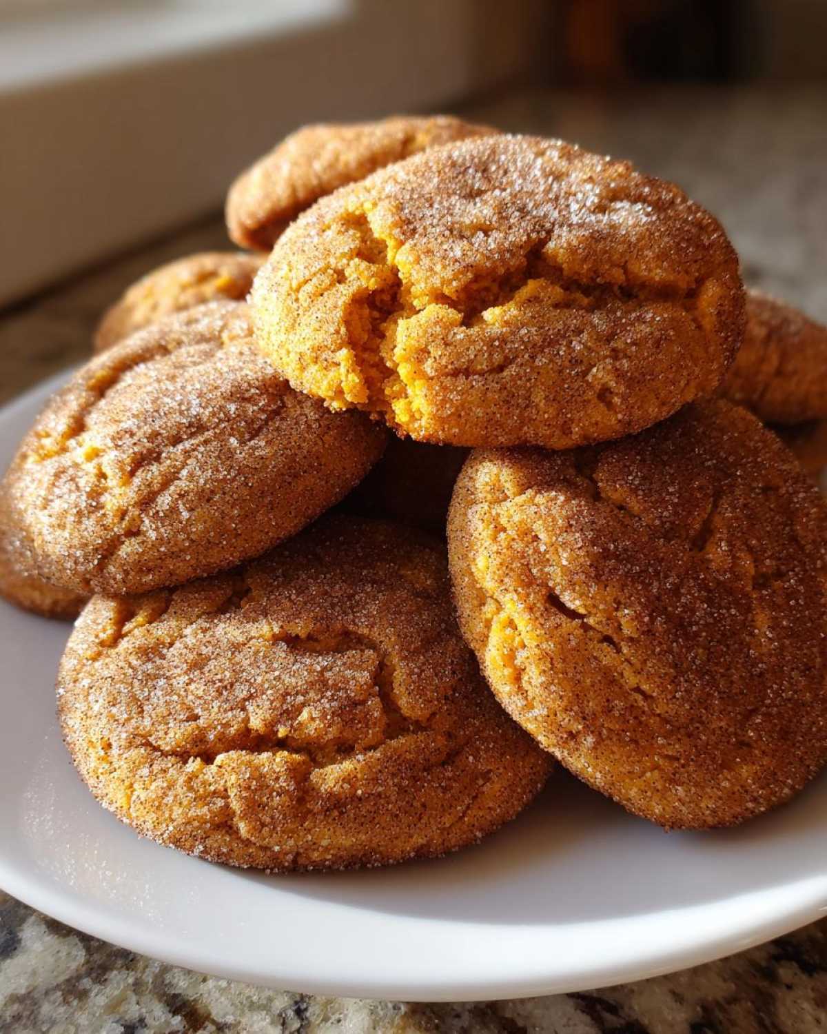 A stack of soft pumpkin snickerdoodle cookies coated in cinnamon sugar, resting on a white plate.
