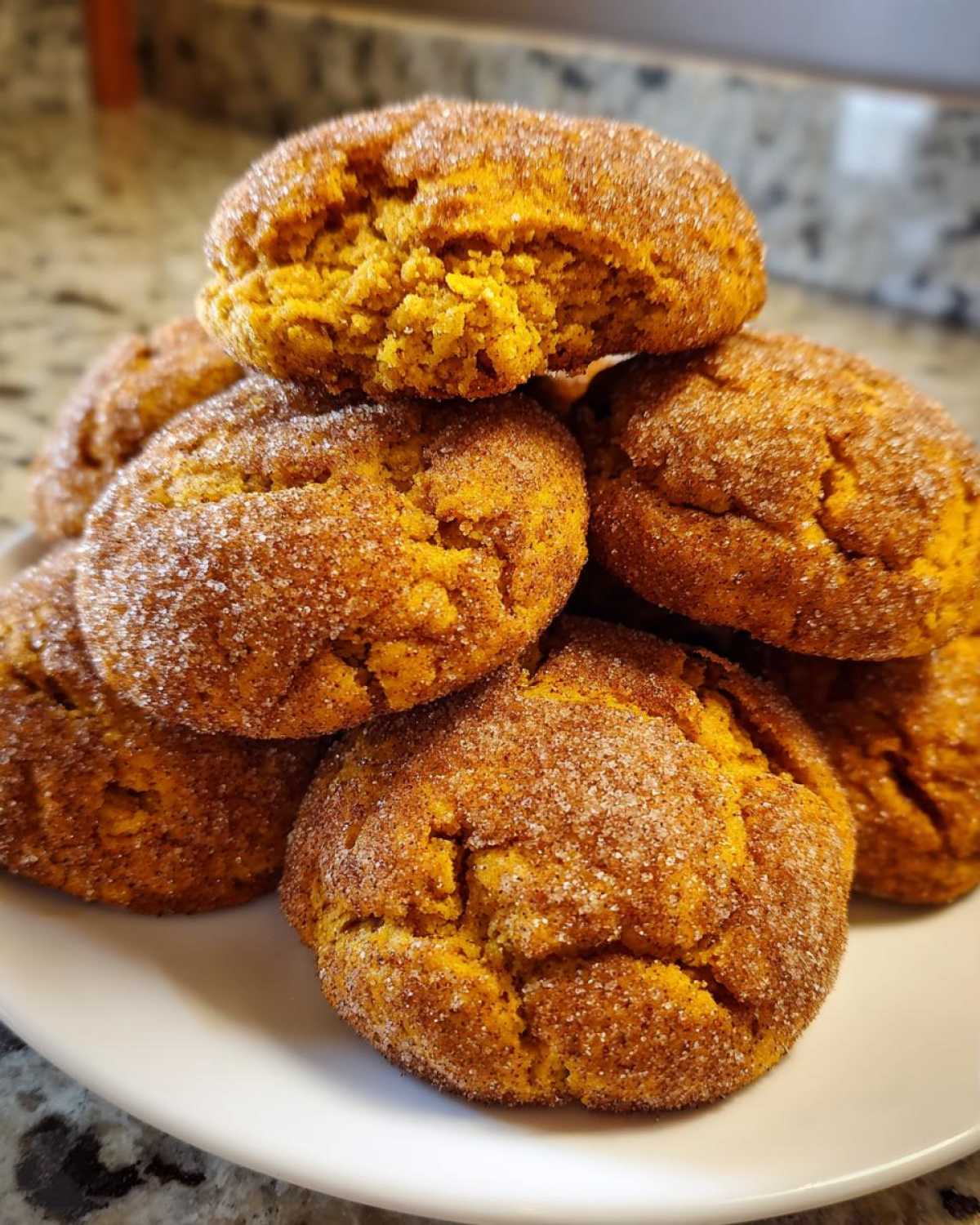 A close-up stack of soft, orange pumpkin snickerdoodle cookies generously coated in cinnamon sugar.