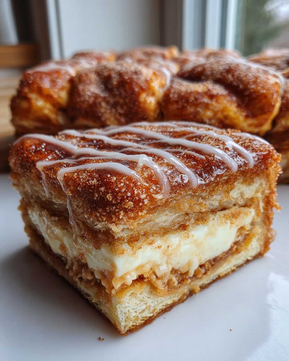 Close-up of a layered slice of sopapilla cheesecake showing creamy filling and cinnamon sugar crust, drizzled with white icing.